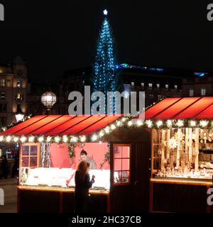 Londra, Grande Londra, Inghilterra, dicembre 15 2021: Persone che frequentano un mercato di Natale a Trafalgar Square con l'albero di Natale regalato dalla Norvegia Foto Stock