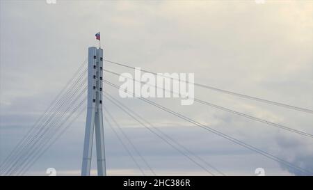 Bandiera della Federazione russa che sbatte nel vento sulla cima del ponte. Bandiera russa sulla cima di un ponte su sfondo grigio e nuvoloso. Foto Stock