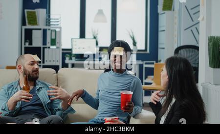 Colleghi felici che giocano a indovinare il gioco per divertirsi dopo il lavoro. I compagni di lavoro allegri che si divertono a giocare con le note appiccicose sulla fronte per divertirsi con le bevande dopo l'orario di lavoro Foto Stock