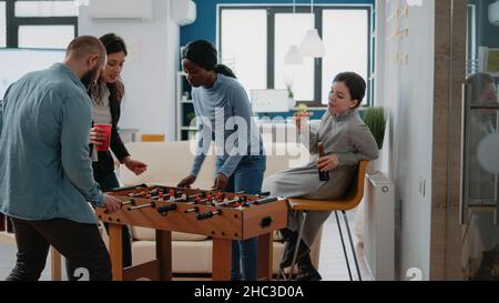 Una squadra di colleghi che si diverse a giocare al tavolo da foosball con bevande e spuntini dopo il lavoro in ufficio. Colleghi che bevono birra e fanno pizza. Divertimento libero attività dopo le ore Foto Stock