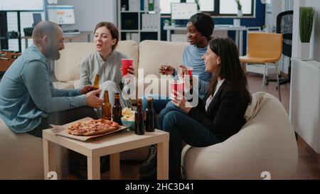 Compagni di lavoro allegri che hanno bevande alcoliche dopo il lavoro in ufficio. I colleghi si godono del tempo libero per un'attività divertente con birra e pizza dopo l'orario di lavoro. Colleghi felici che festeggiano la festa Foto Stock