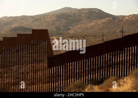 Il tramonto pomeridiano brilla sulle mura di confine tra gli Stati Uniti e il Messico nel centro di Tecate, Baja, Messico. Foto Stock