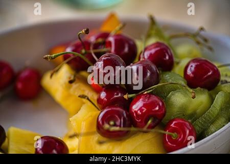 Obstschale mit Kirschen, Ananas und Kiwi als Dessert Foto Stock