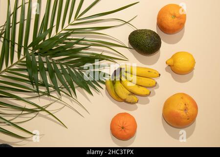 Layout tropicale estivo con frutta fresca e foglie di palma verde su sfondo pastello. Minima superficie piatta naturale. Foto Stock