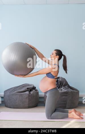 Donna europea incinta esegue esercizi con palla fitness. La madre in attesa sta facendo yoga nel 3° trimestre. Ragazza in classe in Foto Stock