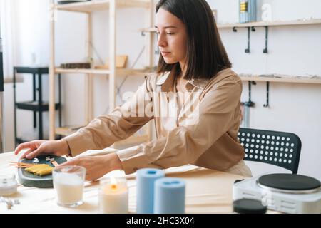 Attraente artigiano femminile preparare spazio di lavoro al tavolo per creare candele fatte a mano in officina. Foto Stock