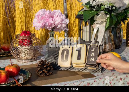 Mano girando pagina su flip vintage calendario metallo cambiare a 1 gennaio, sul tavolo con decorazione partito. Conto alla rovescia per nuovo anno concetto Foto Stock