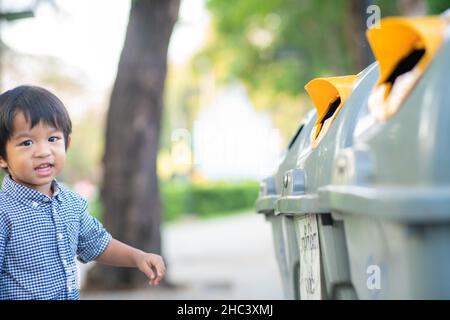 Adorabile ragazzino tenere spazzatura pulita a bin nel parco eco ambientnt concetto Foto Stock