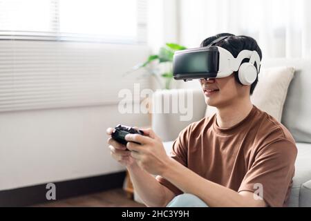 Concetto di tecnologia Un uomo che indossa una cuffia per realtà virtuale e preme un gioco di console nero mentre è seduto sul pavimento. Foto Stock