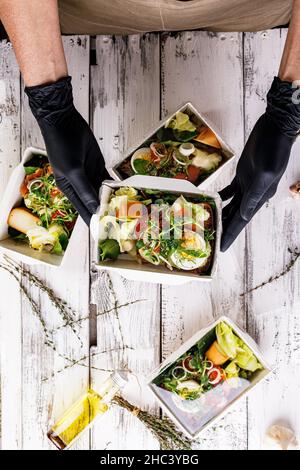 Le mani in guanti neri stanno imballando un pranzo di affari in una scatola di cartone. Concetto di servizio di consegna di cibo. Ristorante take away. Cibo delizioso al lavoro Foto Stock