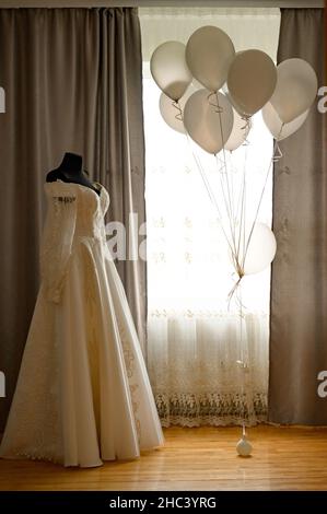 abito della sposa su manichino nero, palloncini intorno, vestito color latte. Foto Stock