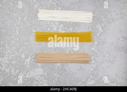 Tre tipi di pasta secca italiana su fondo grigio di cemento. Tagliatelle, spaghetti, tagliatelle di grano saraceno. Vista dall'alto Foto Stock