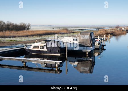 Barche a motore con tenda ormeggiata nell'acqua di un porto in inverno. L'acqua è liscia e il paesaggio e i moli sono coperti di hoarfrost Foto Stock