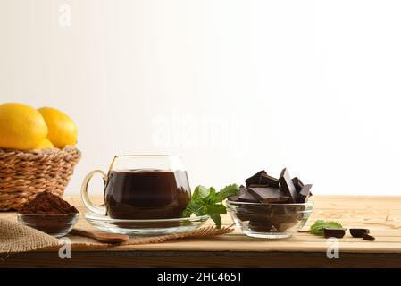 Tazza di cioccolato caldo biologico in bicchiere di vetro su tavola di legno con pezzo e polvere di cioccolato bianco fondo isolato. Vista frontale. Compo. Orizzontale Foto Stock