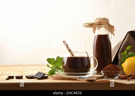 Tazza di cioccolato liquido organico in una tazza di vetro su un tavolo di legno con pezzo e fondo isolato bianco cioccolato. Vista frontale. Compositi orizzontali Foto Stock