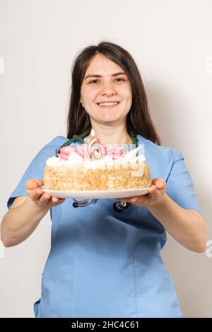 Il medico o l'infermiere tiene una torta di compleanno con il numero sei per l'anniversario dell'apertura della clinica Foto Stock