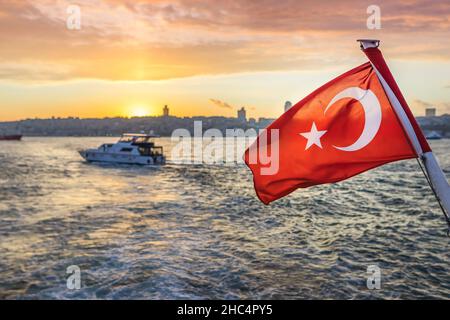 La bandiera turca sventola in barca contro il Bosforo di Istanbul al tramonto. La bandiera della Repubblica di Turchia. Foto Stock