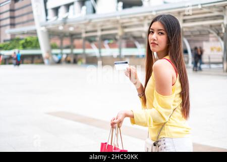 Bella donna asiatica che mostra carta di credito e custodia shopping nel parco della città Foto Stock