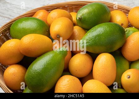 Cestino con calcari freschi verdi interi e kumquat arancioni da vicino Foto Stock