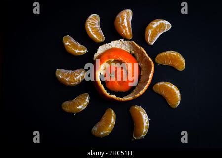 cunei di mandarino organici disposti in cerchio con la buccia a spirale su sfondo di carta nera con spazio per la copia Foto Stock