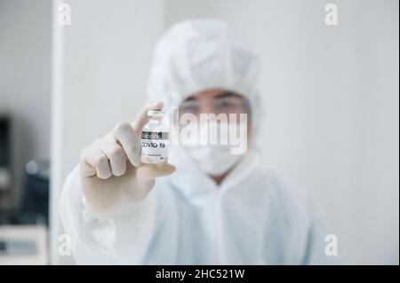 Uomo scienziato in dpi medico protettivo che mostra efficace flacone di vaccino contro Covid-19, Coronavirus in laboratorio Foto Stock