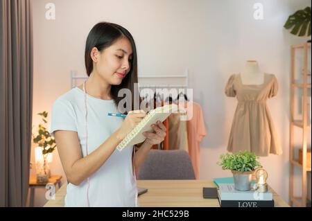 Attraente imprenditore asiatico in piedi e prendendo nota in negozio di abbigliamento online Foto Stock