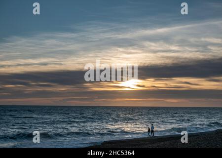Vista al tramonto delle persone che camminano sulla spiaggia di Brighton guardando verso il sole, Brighton, East Sussex, Regno Unito. Foto Stock