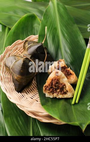 Zongzi o Bakcang (Bacang). Gnocchi di riso Sticky cinese in foglie di bambù. Servito su piatto di rattan. Una metà e mostrato carne (maiale, Foto Stock