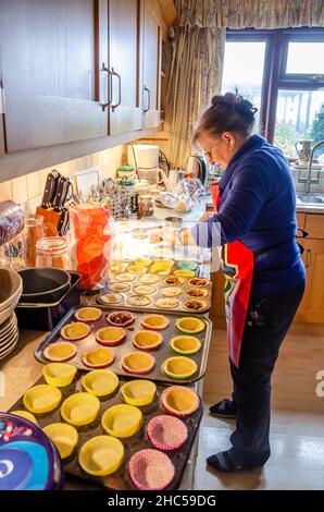 Una donna che fa torte di mince a casa in una cucina. Le scatole di cupcake sono disposte sul piano di lavoro della cucina. Foto Stock