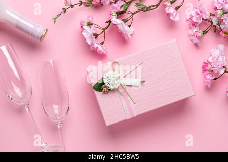 Fiori primaverili, bicchieri, champagne e confezione regalo su sfondo rosa festivo. Biglietto di auguri romantico il giorno di San Valentino. Giornata internazionale della donna, ce Foto Stock