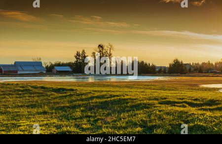Bellissimo tramonto in zona rurale con piccolo villaggio e fiume con cielo drammatico durante la stagione autunnale. Vista sulla strada, foto di viaggio, fuoco selettivo, nessuno Foto Stock