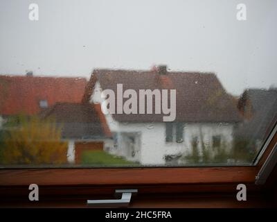 Primo piano di vetro della finestra con gocce di pioggia, case residenziali non focalizzate sullo sfondo Foto Stock