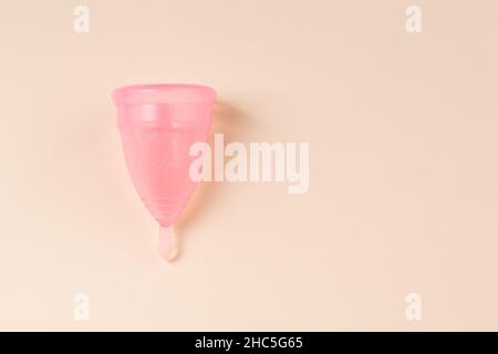 Tazza mestruale rosa su sfondo beige chiaro. Prodotto per l'igiene femminile ecologico alternativo. Spazio di copia. Foto Stock