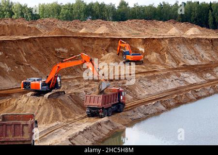 Caricamento della sabbia nei camion sulla carriera sabbiosa, minerario. Escavatori e autocarri Foto Stock