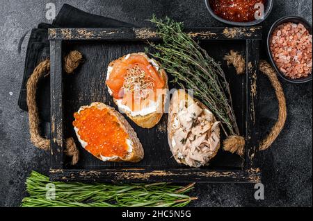 Sandwich con salmone affumicato caldo e caviale rosso, pane tostato con formaggio cremoso. Sfondo nero. Vista dall'alto Foto Stock