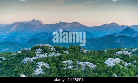 Prominente area montagnosa del Montenegro che circonda il monte Lovcen e il Mausoleo di Njegos con colline stratificate, foschia nebbiosa al tramonto Foto Stock