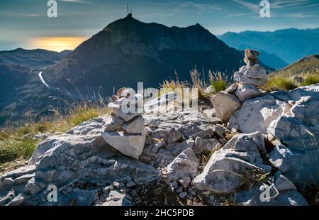 Piccole pile di pietre, creativamente costruito nel tempo da visistori al Mausoleo Njego, Lovcen Parco Nazionale, guardando a ovest, retroilluminato dal tramonto del sole in Foto Stock