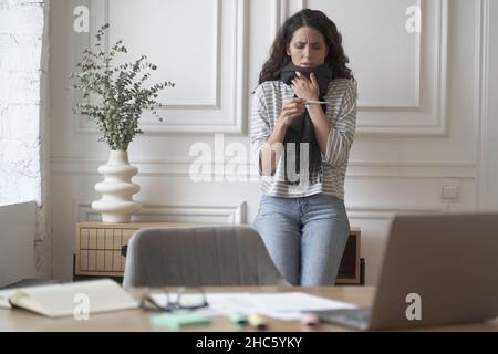 Donna malata lavoratore freelance con febbre che misura la temperatura elevata mentre lavora a distanza a casa Foto Stock