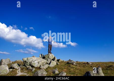 un solo uomo si alza con le braccia tese su una roccia contro un cielo blu Foto Stock