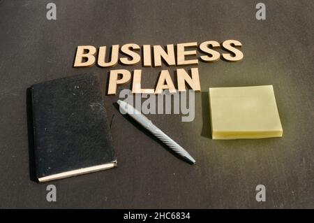 Businessman mano mettendo una penna e un taccuino di fronte al piano di Business di Word fatto di blocchi di legno di lettere Alphabet. Vista ad angolo alto. Retro verticale Foto Stock