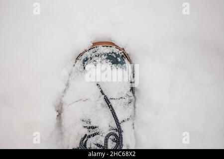 Primo piano di foto di inverno blu caldo stivale con lacci fuori nella neve facendo impronta a terra coperto di neve. Sfondo sorprendente pieno di bianco e. Foto Stock