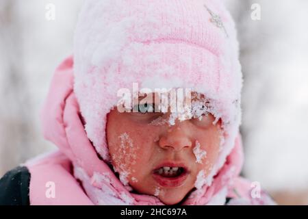 Primo piano foto di femmina capretto con triste volto coperto di neve e sul punto di piangere indossando abiti rosa inverno nella foresta. Sfondo sorprendente pieno di Foto Stock