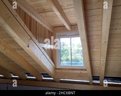 Struttura in legno di una capriate tetto con finestra dormer nel piano attico di un nuovo edificio residenziale, lavori di costruzione prima dell'interno c Foto Stock