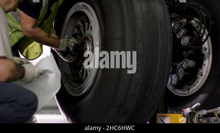 Riparazione dei freni degli aerei. Primo piano della ruota dell'aeroplano e dell'albero. Enorme pneumatico di aeroplano con albero e ingranaggio di atterraggio di aereo sotto l'aeroplano. Fissaggio tecnico a Foto Stock