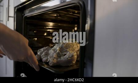 Cuocere in forno il pollo crudo con un condimento di maionese bianco. Concetto di cottura domestico, primo piano delle mani che mettono il pollo con rosmarino nell'ov Foto Stock