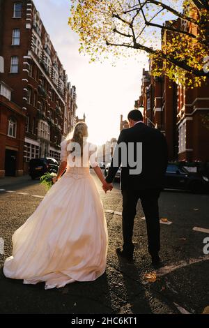 Crop sposa e sposo tenere le mani e camminare sulla strada Foto Stock