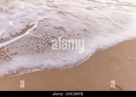 Giornata di sole sulla spiaggia con maree di mare poco profonde e schiumose che si lavano sulla sabbia Foto Stock