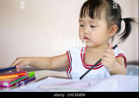 Una giovane femmina asiatica toddler con i capelli neri è sorridente.She felice con matite colorate.e spazio di copia. Foto Stock