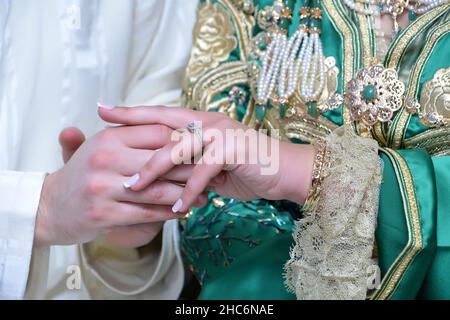 Lo sposo marocchino indossa l'anello di nozze della sposa. Sposa marocchina in verde caftan marocchino Foto Stock