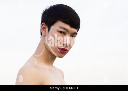 Un uomo gay asiatico bello che non indossa una camicia, scrive sul viso e indossa un rossetto rosa. Spazio di copia Foto Stock